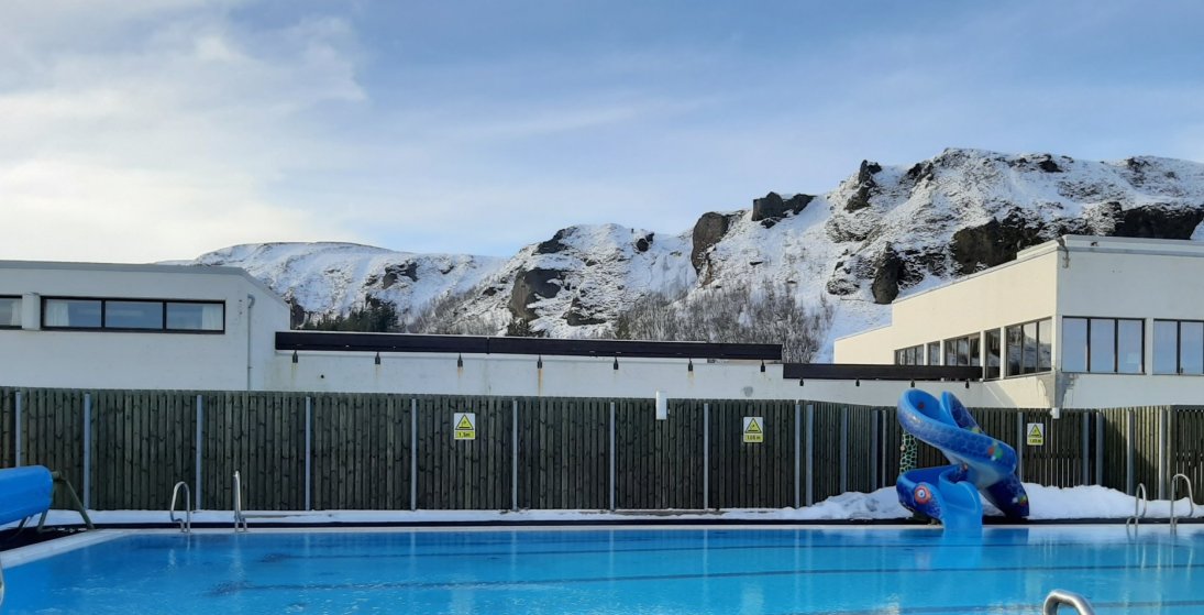 Sundlaugin á Kirkjubæjarklaustri og frosinn Systrafoss í baksýn